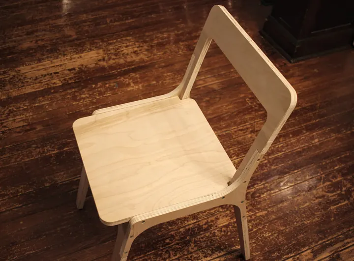 A sheet-cut plywood chair on a dark wood floor