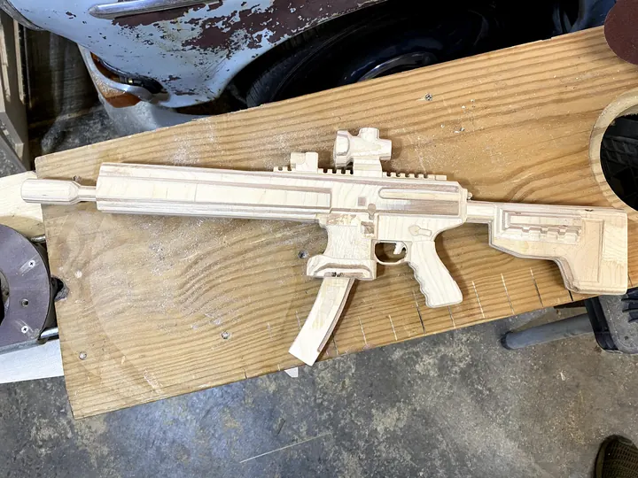 A wooden rifle replica cut from plywood, on the bed