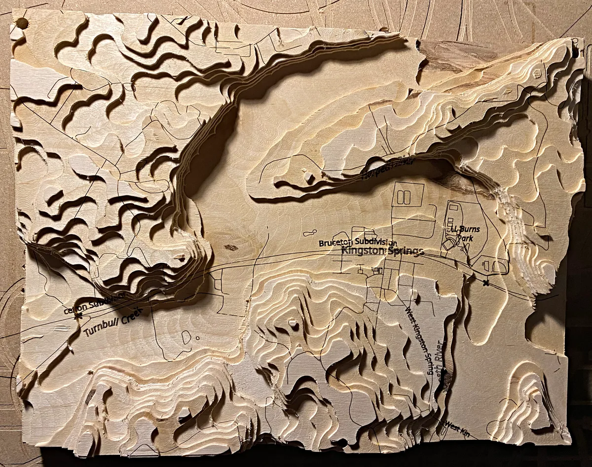 A carved wooden topographic map shows layered hills, waterways, and engraved place names.